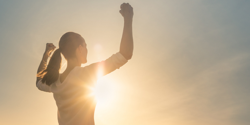 A young woman with arms flexed facing the sunset illustrate empowerment in health, wellness and social care.