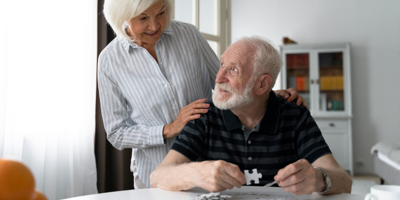 A caring woman assists a senior with Alzheimer's as he works on a puzzle.